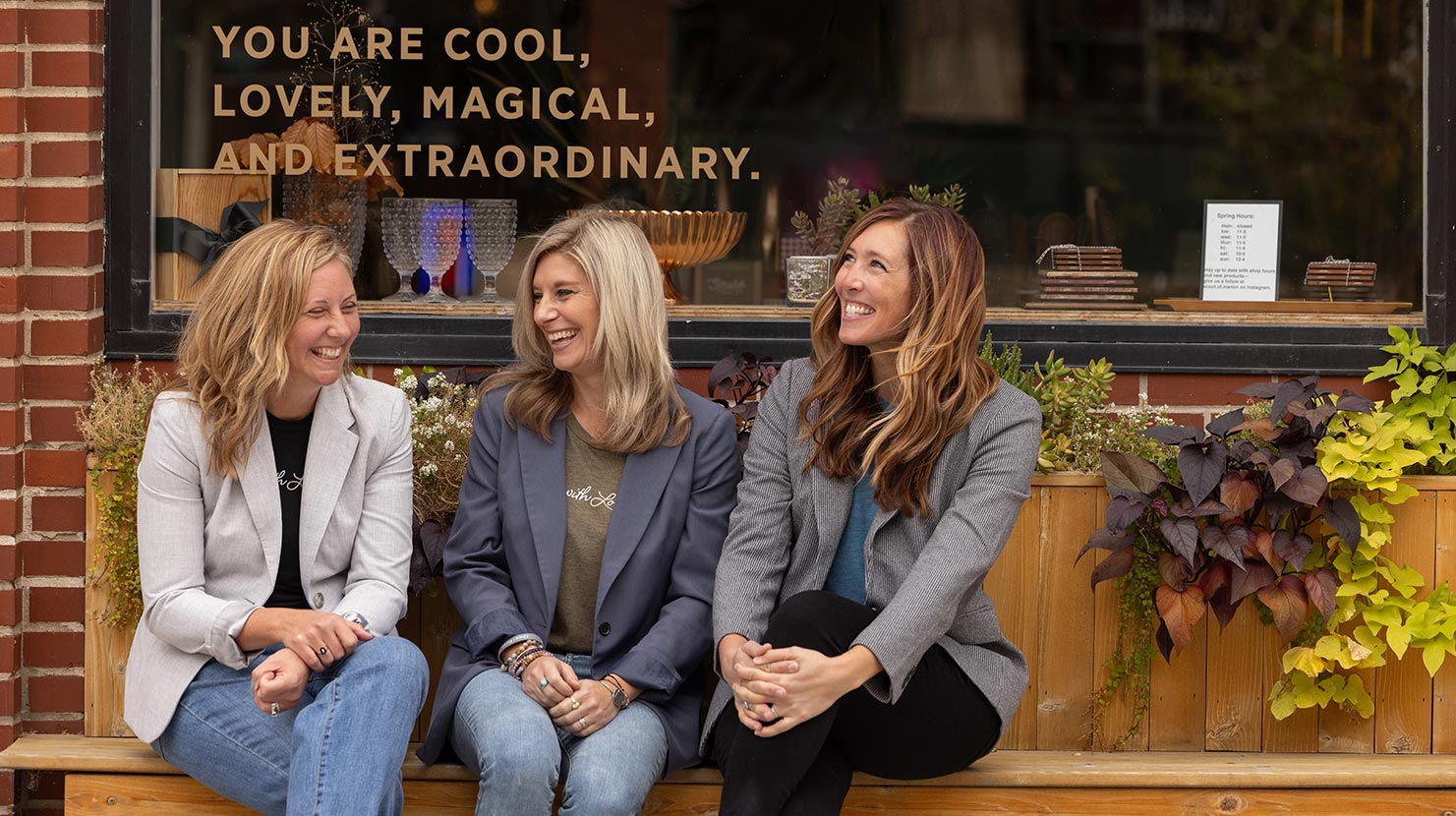 Brooke, Lindsay, and Sara sit on a bench in front of a store