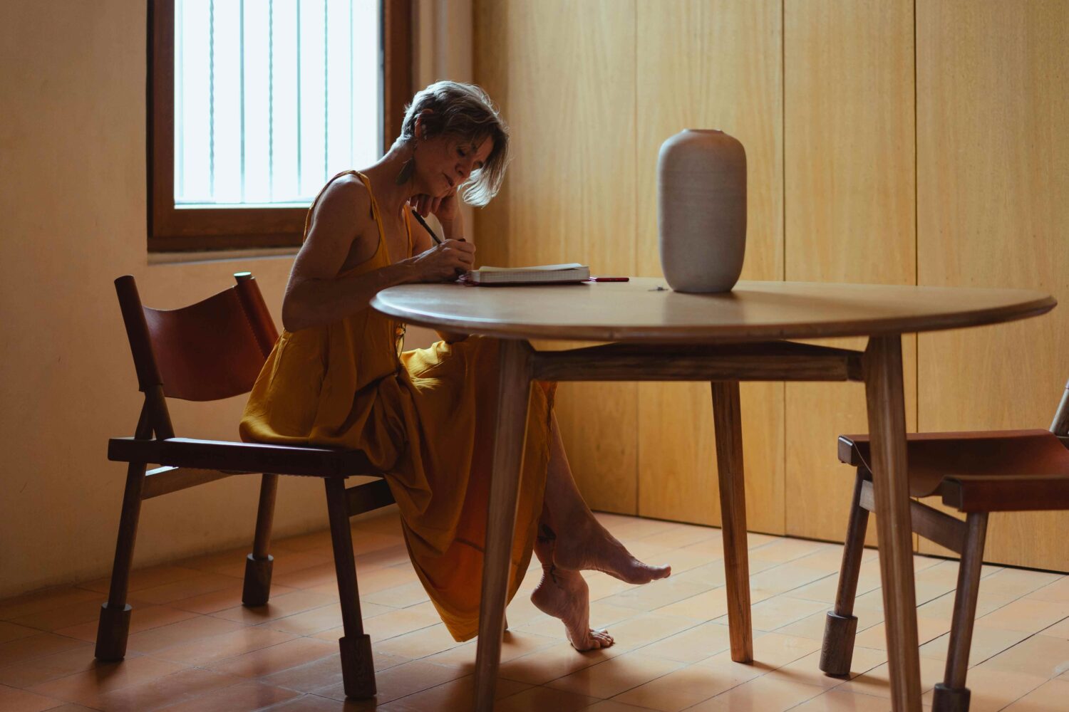 mid-life woman journaling at a round table in a warm, wood-paneled room