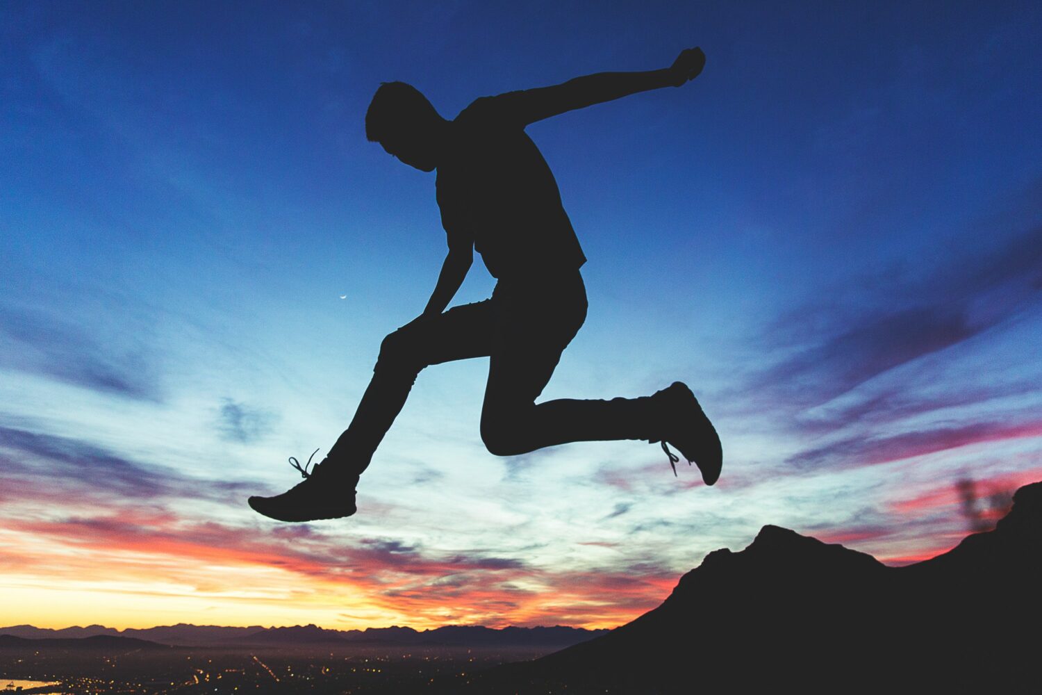 a person jumps over rocks during a beautiful sunset